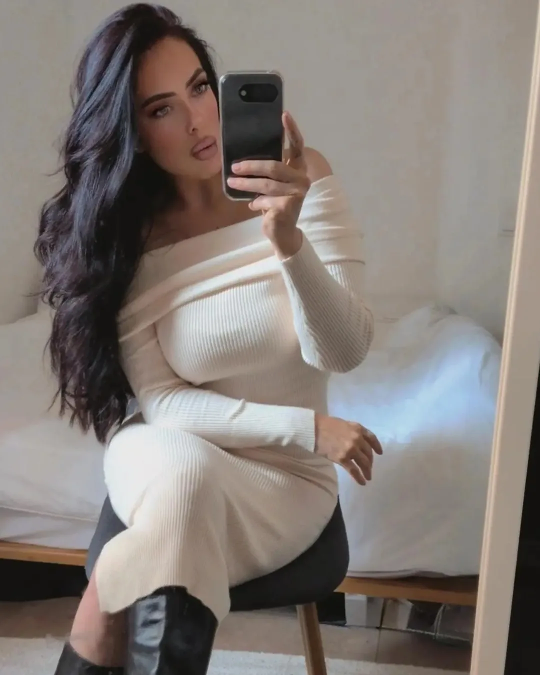 Beige off shoulder-stickad klänning och svarta stövlar i en spegelselfie.