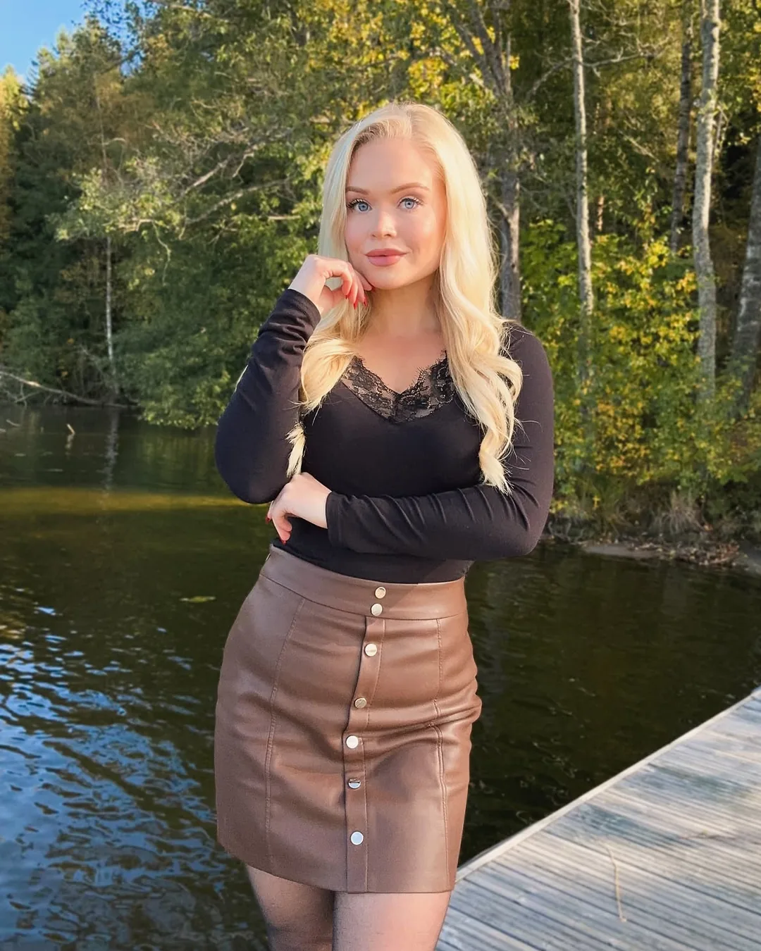 Svart långärmad v-ringad blus med spets och brun kjol med knappar i en höstbild utomhus.