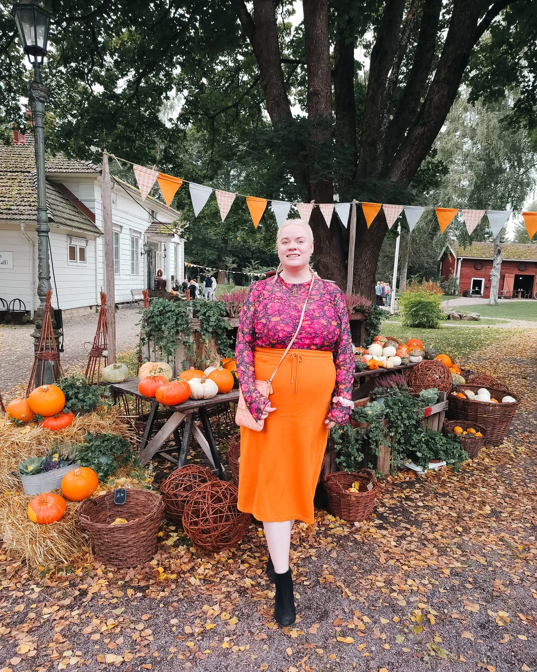 @deluxedesiresfi i en rosa långärmad blommig meshtopp och orange kjol utomhus.